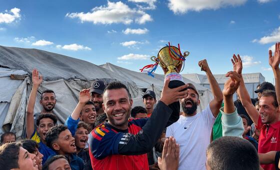 لاعب كرة القدم الفلسطيني أسعد العزابي يحمل كأس بطولة مخيمات نازحي رفح، يحتفل مع حشد من الشباب والأطفال في مواصي خان يونس.